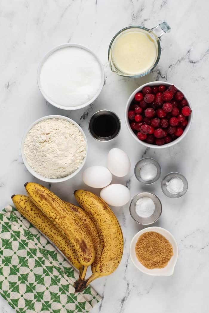 Ingredients for cranberry banana bread arranged on a marble countertop.