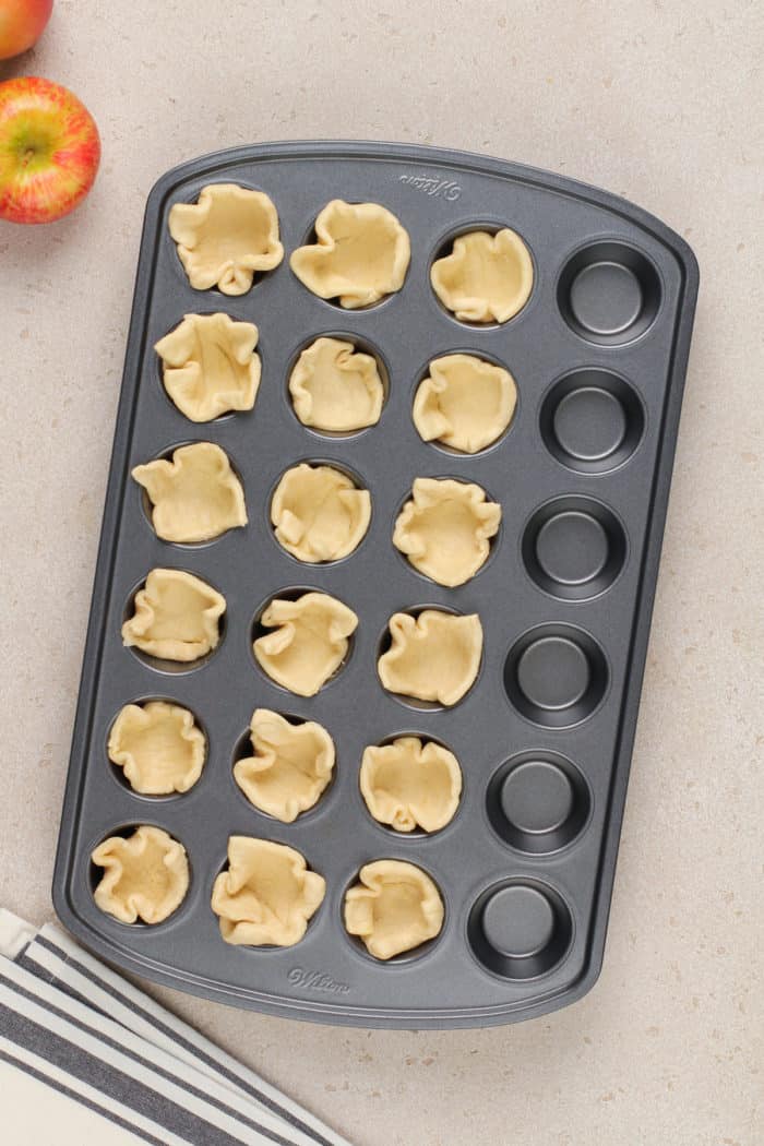 Pieces of crescent roll dough formed into cups in a mini muffin pan.