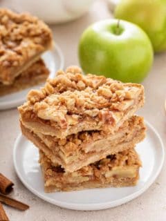 Three apple crisp bars stacked on a white plate. The top bar has a bite taken from the corner.