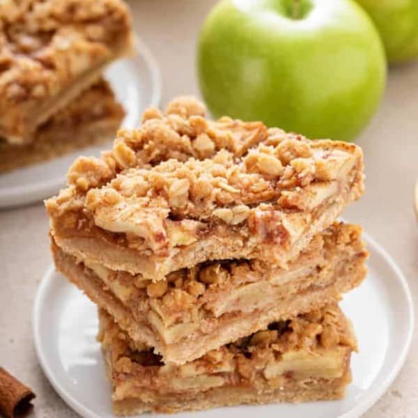 Three apple crisp bars stacked on a white plate. The top bar has a bite taken from the corner.