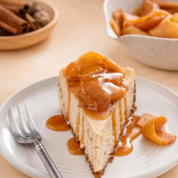 Front view of a slice of caramel apple cheesecake on a plate next to a fork.