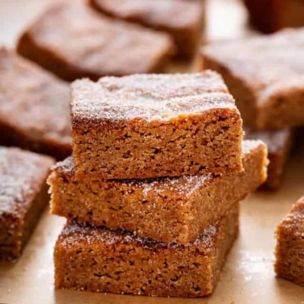 Three apple cider blondies stacked in a piece of brown parchment paper.