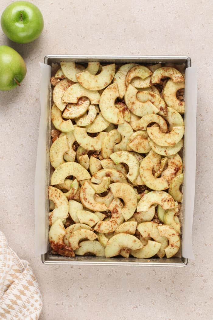 Apple filling added to apple crisp bars in a parchment-lined pan.