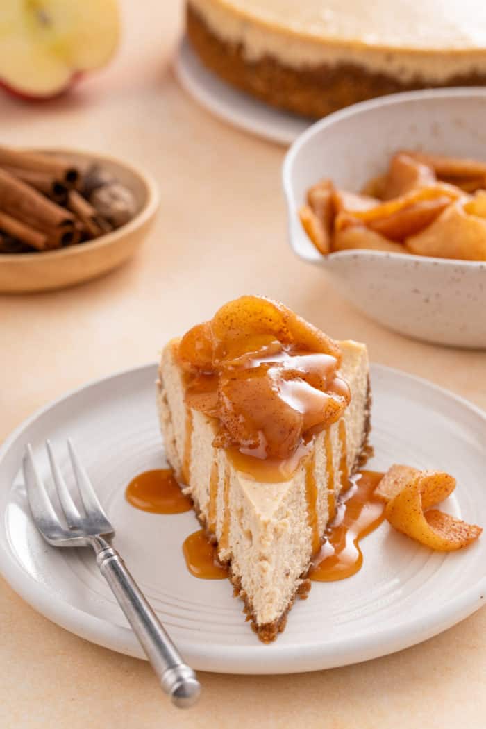 Front view of a slice of caramel apple cheesecake on a plate next to a fork.