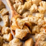 Wooden spoon scooping up homemade croutons from a baking sheet.