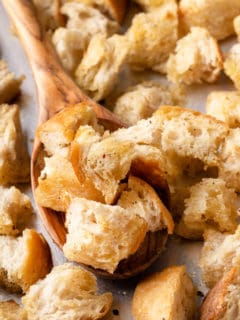 Wooden spoon scooping up homemade croutons from a baking sheet.
