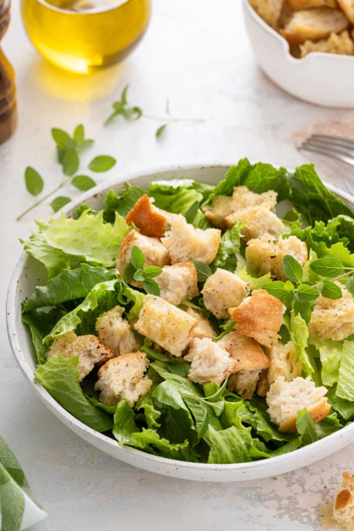 Croutons on top of a green salad in a big, white bowl.