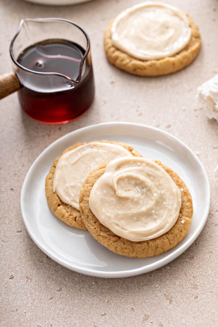 Two frosted maple cookies arranged on a white plate.
