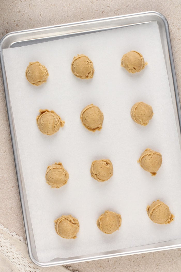 Portioned balls of maple cookie dough on a lined baking sheet, ready to go in the oven.