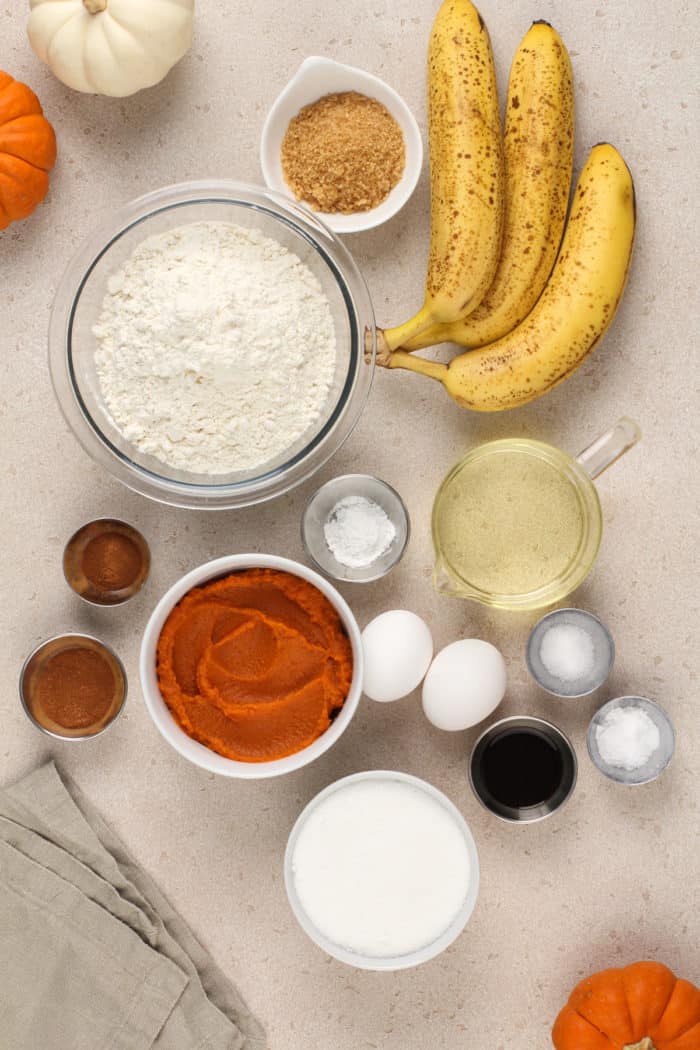 Ingredients for pumpkin banana bread arranged on a beige countertop.