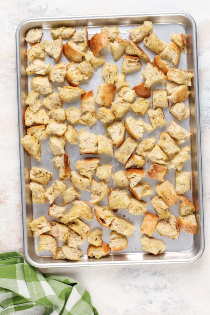 Seasoned chunks of bread on a rimmed baking sheet, ready to go in the oven.