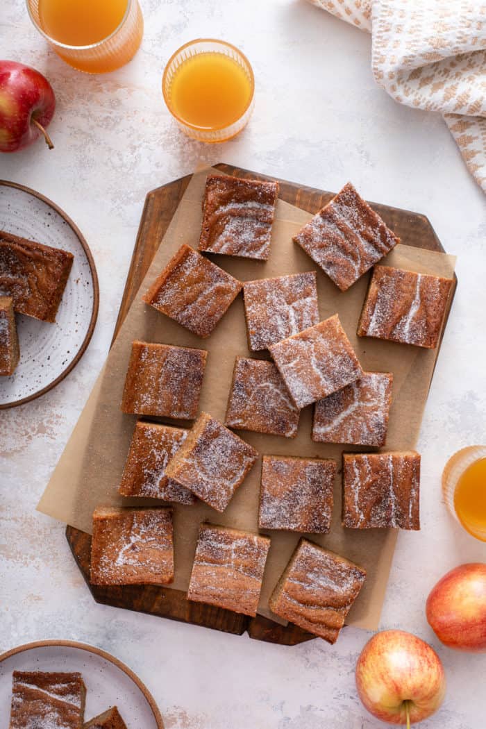 overhead view of sliced apple cider blondies arranged on a wooden cutting board and piece of parchment paper.