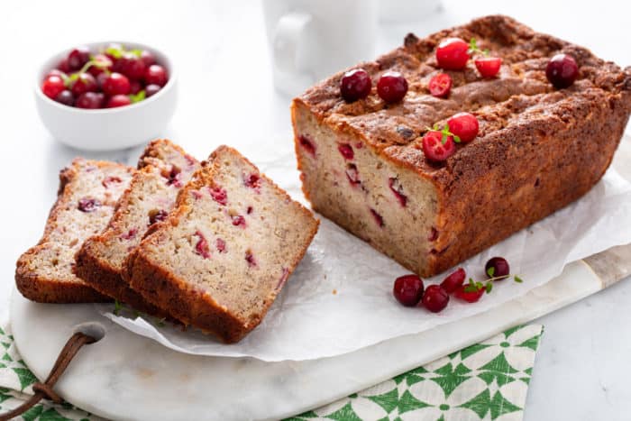 Sliced loaf of cranberry banana bread set on a marble board and garnished with fresh cranberries.