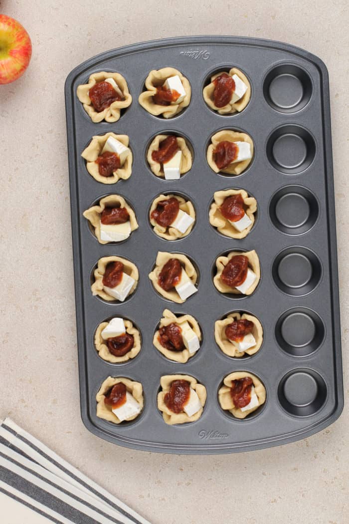 Assembled apple butter brie bites in a mini muffin pan, ready to go in the oven.