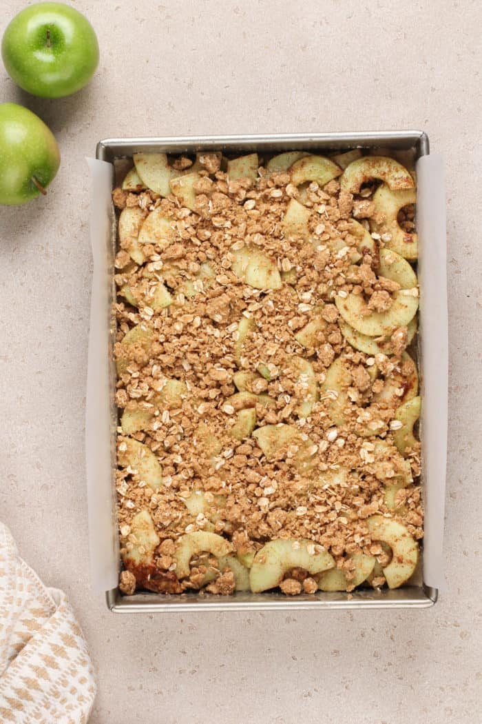 Assembled apple crisp bars in a parchment-lined pan, ready to go in the oven.