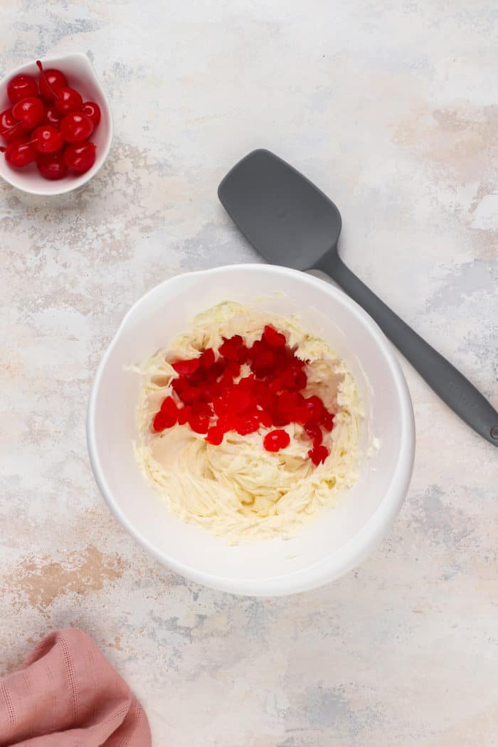 Chopped maraschino cherries about to be folded into whipped butter in a white bowl.