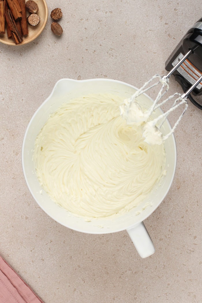 Cream cheese whipped with a hand mixer in a white bowl.