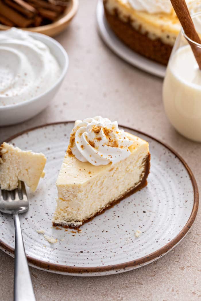 Slice of eggnog cheesecake with a bite taken from it. A fork with the bite of cheesecake is next to it on the plate.