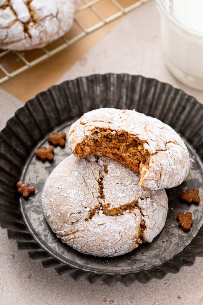 Two gingerbread crinkle cookies in a mini tart pan. One cookie has a bite taken from it.