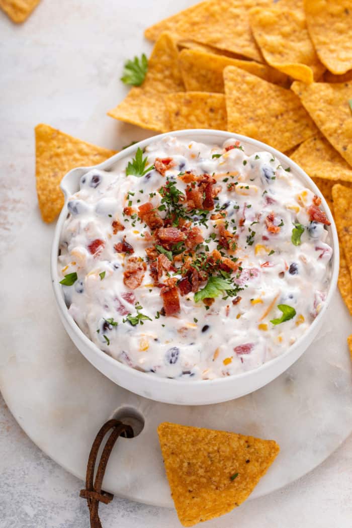 Close up of fiesta ranch dip in a white bowl, garnished with green onions and bacon bits.