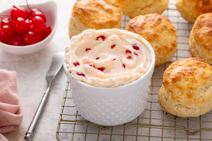 Bowl of whipped cherry butter sitting on a wire rack, surrounded by biscuits.