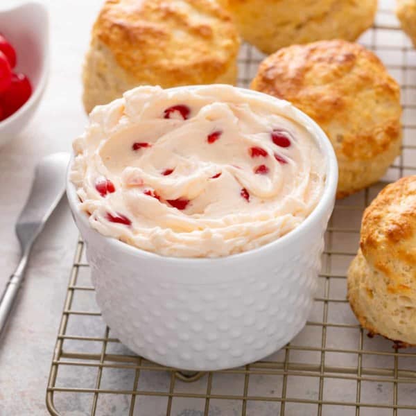 White bowl filled with whipped cherry butter set on a wire rack of biscuits.