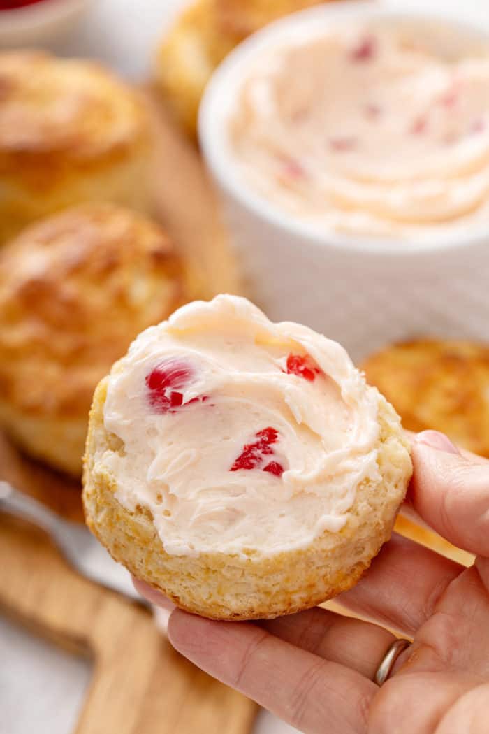 Hand holding up half a biscuit topped with whipped cherry butter.