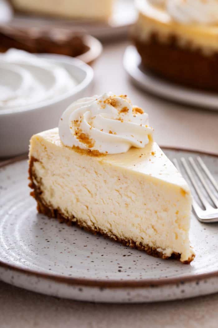 Close up of a slice of eggnog cheesecake topped with whipped cream on a stoneware plate.