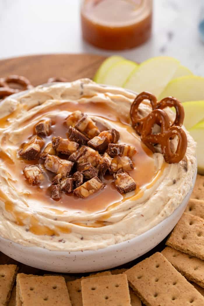 Close up image of a bowl of snickers dip with pretzels stuck in it.