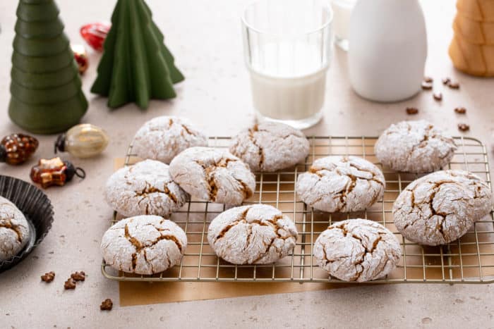 Gingerbread crinkle cookies arranged on a wire cooling rack, with a glass of milk in the background.