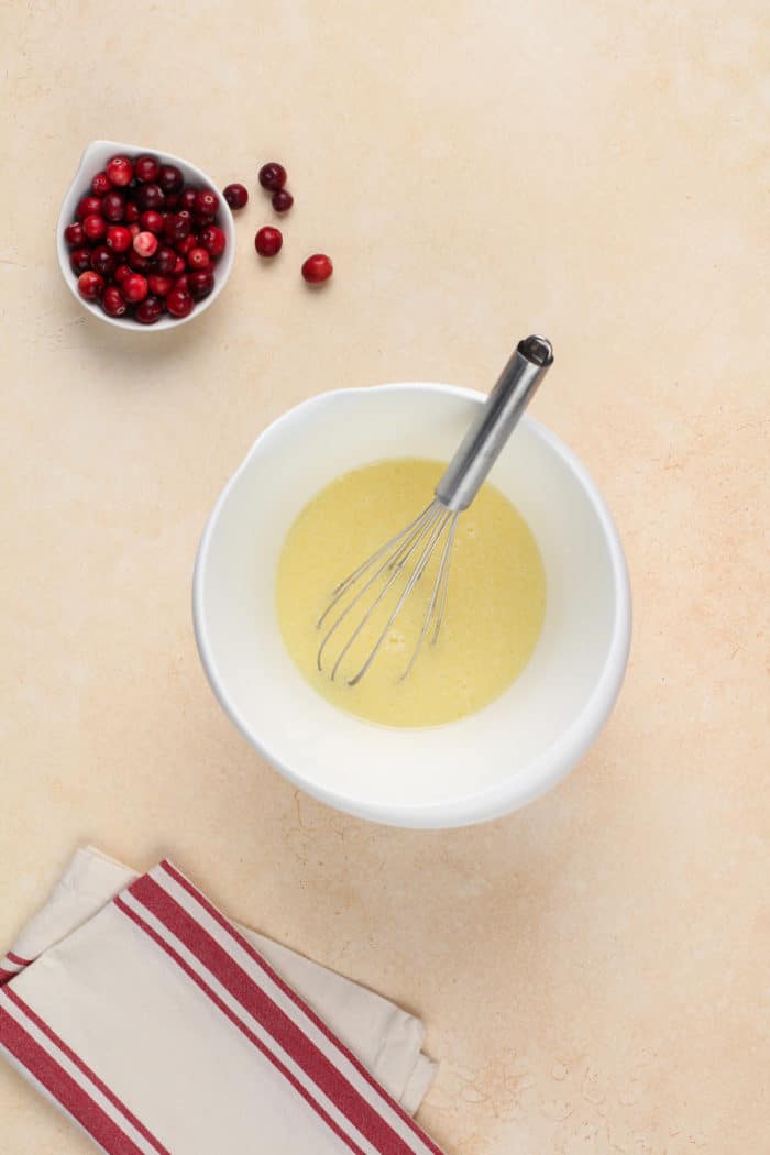 Wet ingredients for cranberry orange muffins whisked in a white bowl.