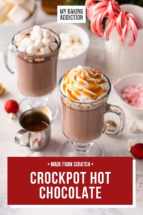 Two glass mugs filled with crockpot hot chocolate and surrounded by various toppings, including peppermints, marshmallows, and caramel sauce. Text overlay includes recipe name.