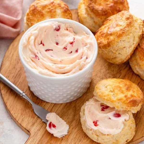 Bowl of whipped cherry butter on a wooden board next to a biscuit topped with the cherry butter.