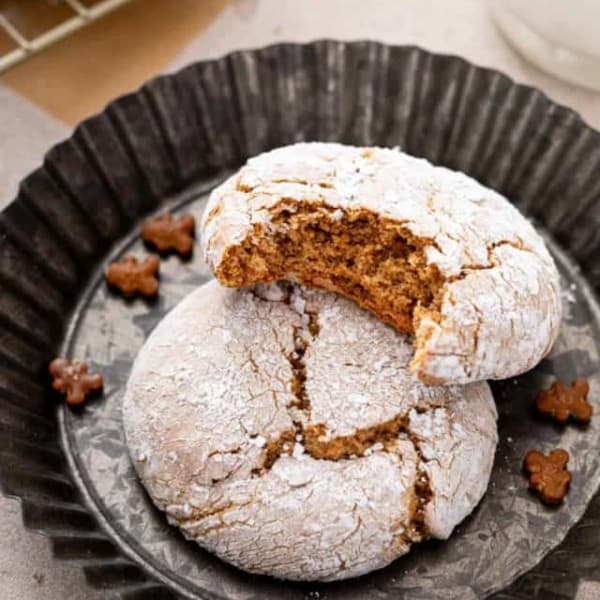 Two gingerbread crinkle cookies in a mini tart pan. One cookie has a bite taken from it.