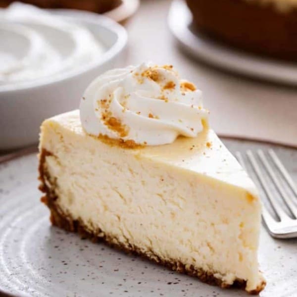 Close up of a slice of eggnog cheesecake topped with whipped cream on a stoneware plate.