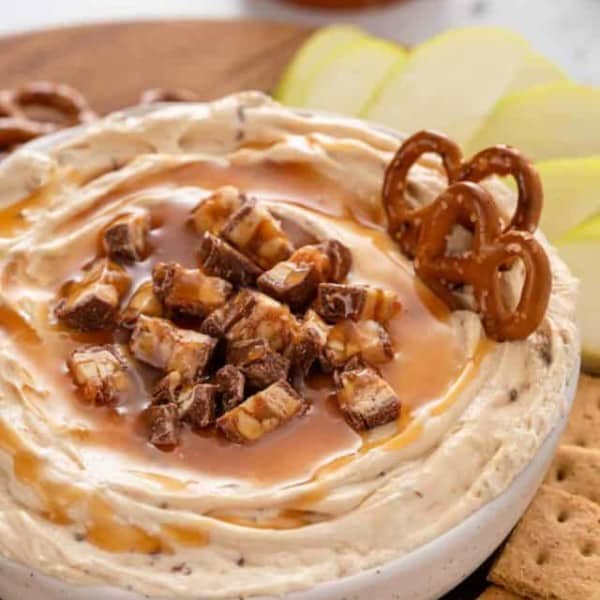 Close up image of a bowl of snickers dip with pretzels stuck in it.