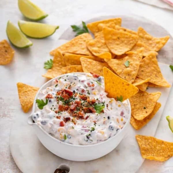 White bowl of fiesta ranch dip on a marble board next to Doritos tortilla chips.