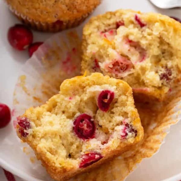 Halved cranberry orange muffin on a white plate next to a whole muffin.