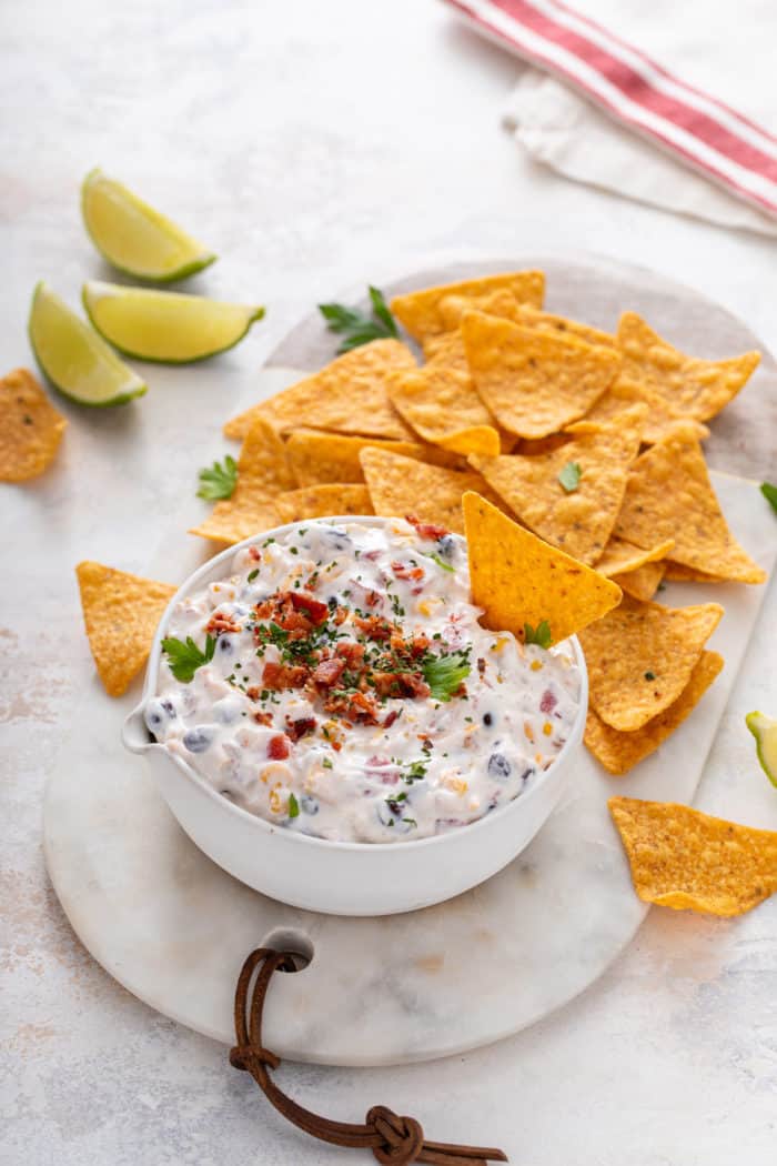 White bowl of fiesta ranch dip on a marble board next to Doritos tortilla chips.