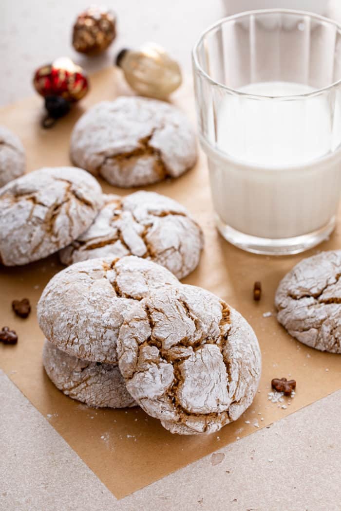 Gingerbread crinkle cookies scattered on a piece of parchment paper around a glass of milk.