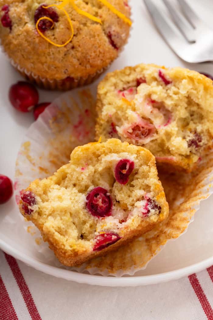 Halved cranberry orange muffin on a white plate next to a whole muffin.