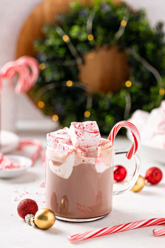 Mug of hot chocolate topped with peppermint marshmallows, with a bowl of the marshmallows in the background.