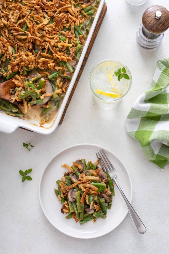 Overhead view of a white plate with fresh green bean casserole next to a casserole dish filled with green bean casserole.