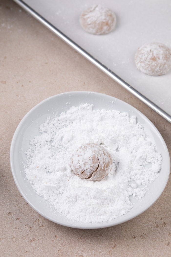 Ball of gingerbread crinkle cookie dough being rolled in powdered sugar.
