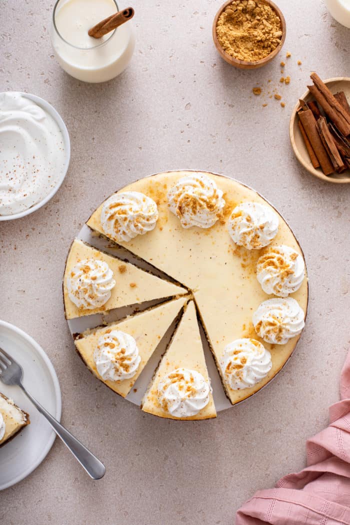 Overhead view of a sliced eggnog cheesecake garnished with whipped cream.