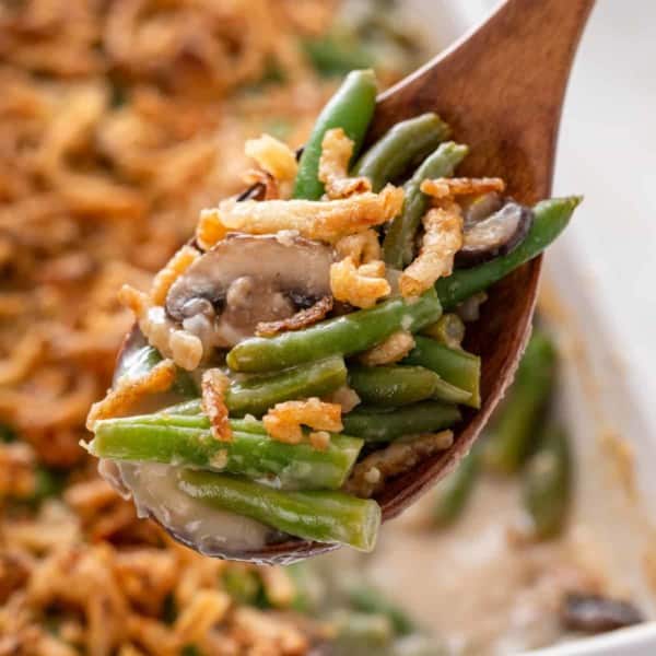 Wooden spoon holding up a spoonful of fresh green bean casserole.