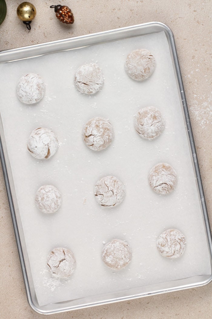 Unbaked gingerbread crinkle cookies on a parchment-lined baking sheet.