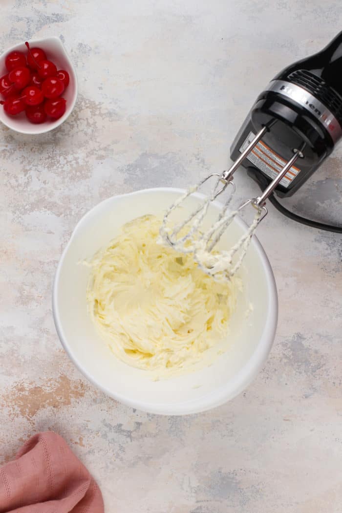 Whipped butter and sugar in a white bowl next to an electric mixer.