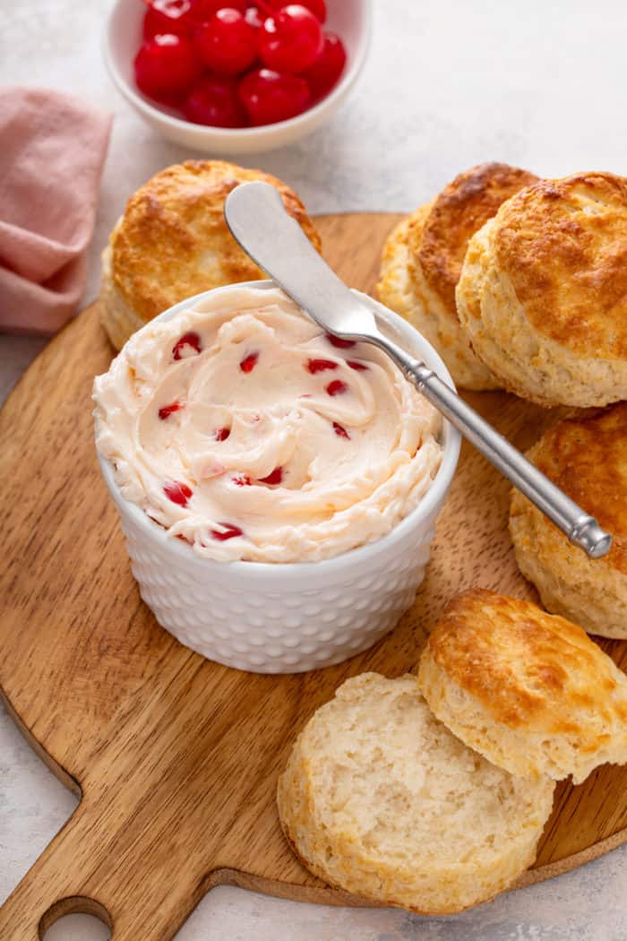 Bowl of whipped cherry butter on a wooden board, surrounded by biscuits.