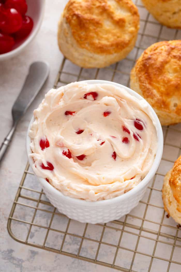 Close up of a bowl of whipped cherry butter on a wire rack next to biscuits.